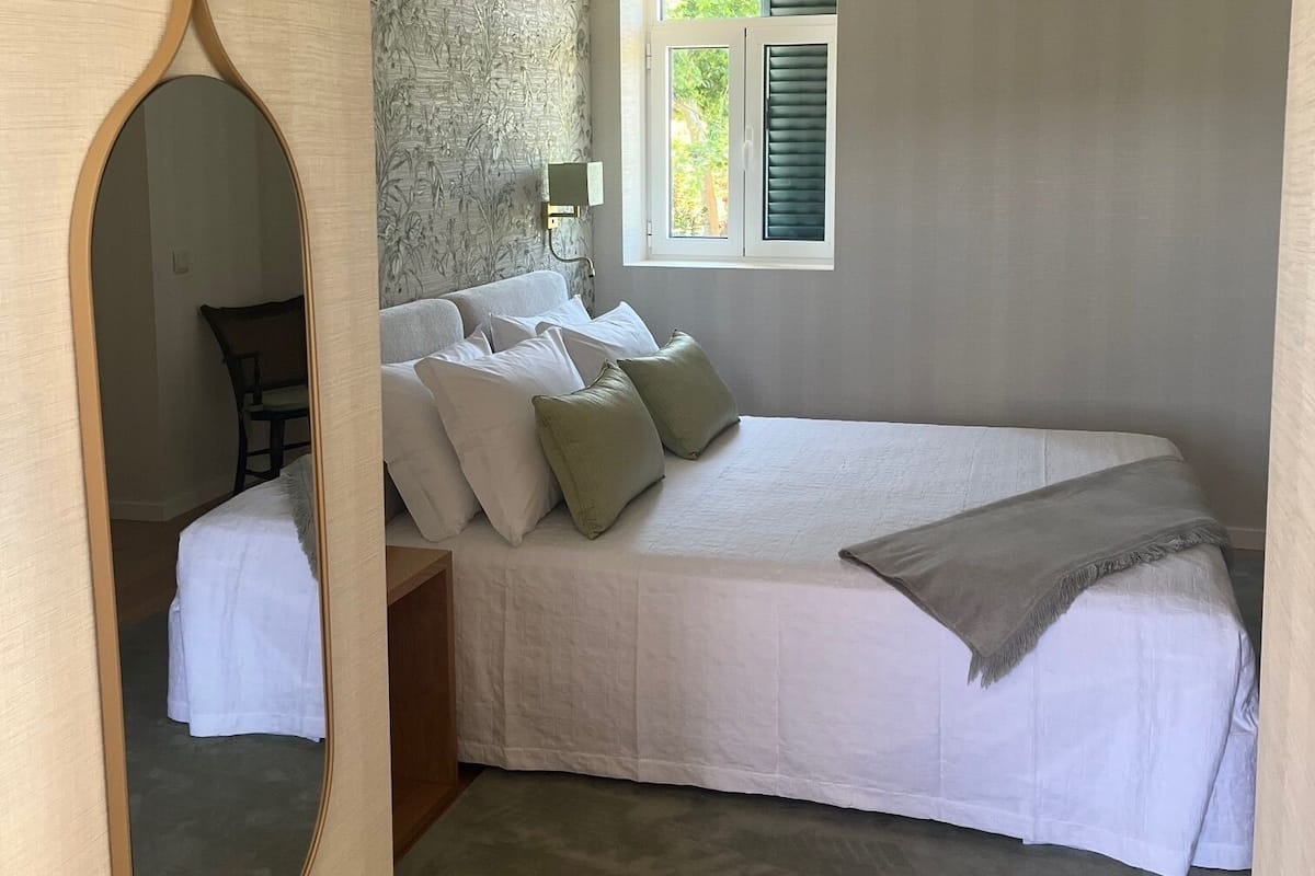 A bedroom with a bed, a window, a mirror, and a nightstand.