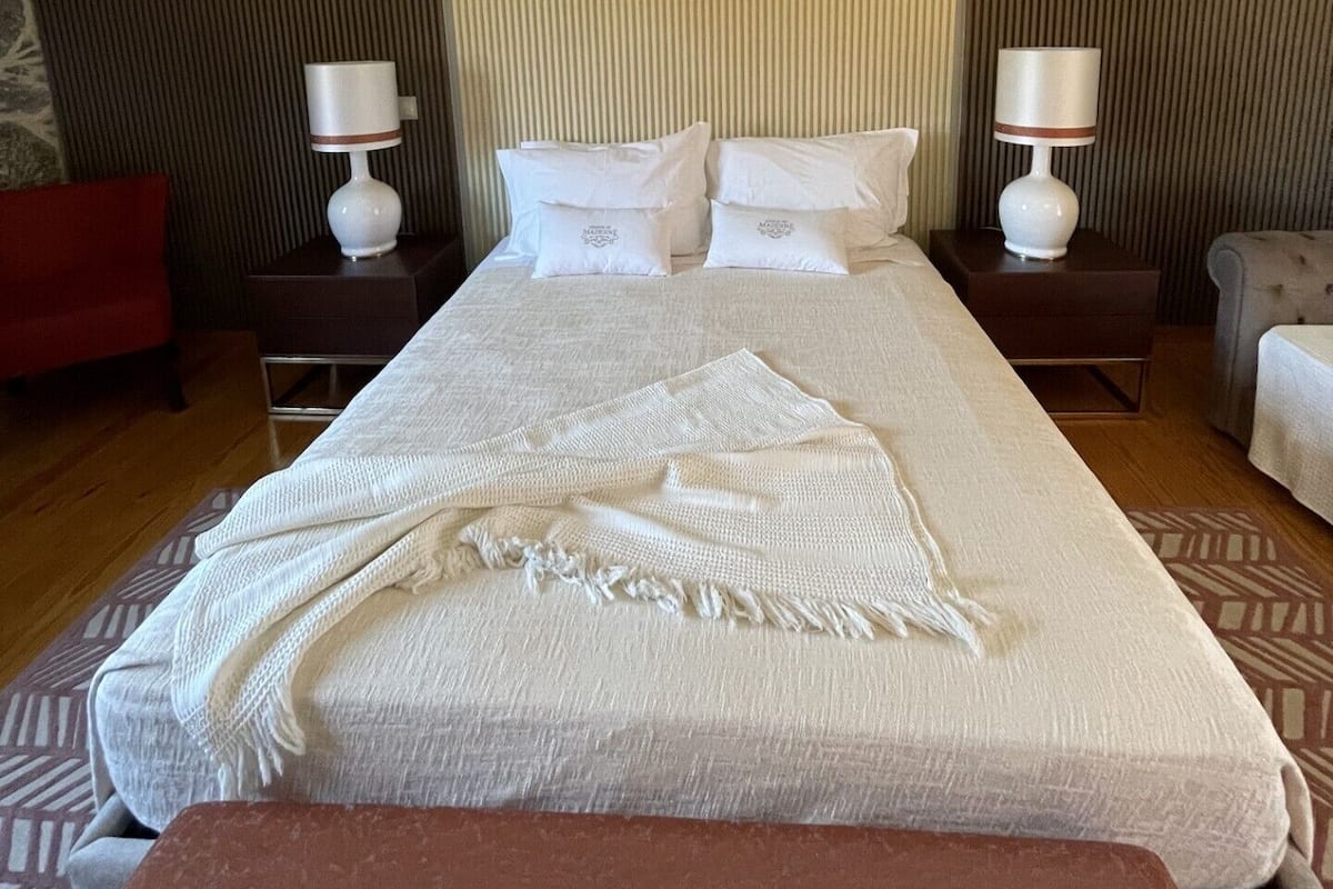 A hotel room with a large bed, two bedside tables with lamps, a red armchair, and a patterned rug.
