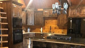 A kitchen with wooden cabinets, a large island with bar stools, and a stone backsplash. - Relax, Fish, Visit Historic Jefferson & Caddo Lake (Jefferson)