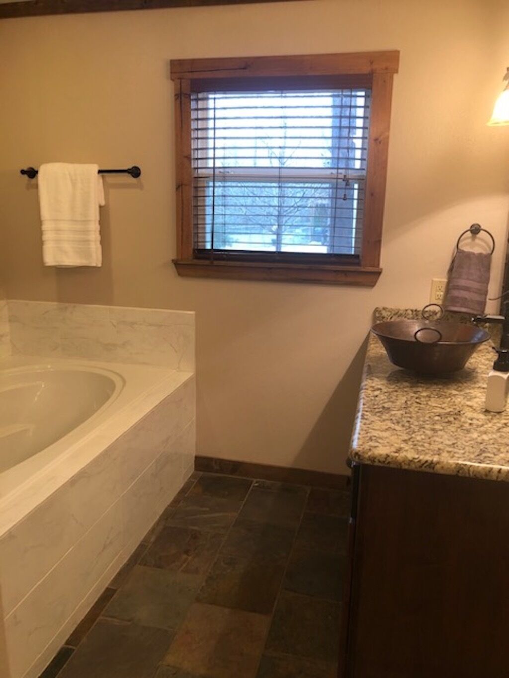 A bathroom with a bathtub, a window with blinds, a towel rack, and a sink with a bowl.