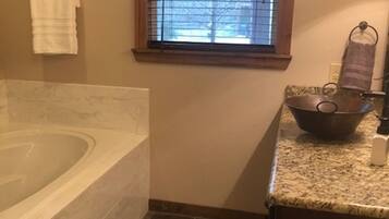 A bathroom with a bathtub, a window with blinds, a towel rack, and a sink with a bowl.