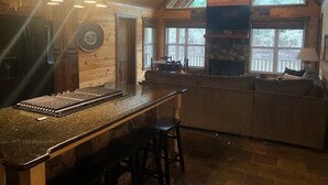A cozy cabin interior with a bar area, stone fireplace, and large windows. - Relax, Fish, Visit Historic Jefferson & Caddo Lake (Jefferson)