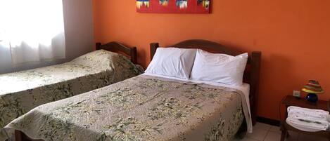 A room with two beds, each with floral bedding, a painting on the wall, and a nightstand with a lamp and towels.