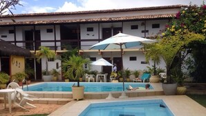 Un espace piscine doté de chaises longues et de parasols, entouré de plantes en pot et bordé d’un bâtiment dont le toit est recouvert de tuiles.