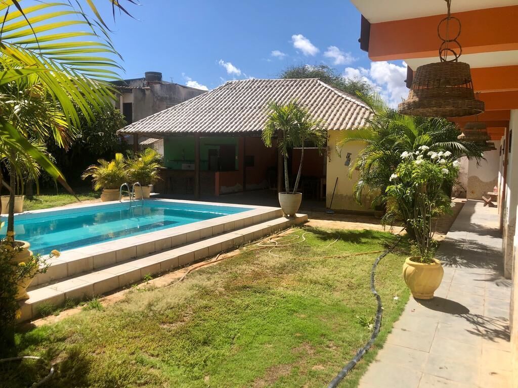 A backyard with a swimming pool, potted plants, and a house with a tiled roof.