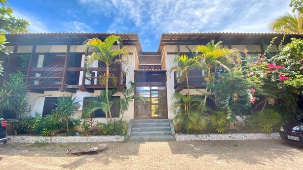 Un bâtiment à deux étages, doté d’une entrée carrelée, entouré de plantes tropicales et surplombé d’un ciel dégagé.