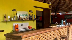 Un coin bar avec un comptoir en briques, une étagère remplie de bouteilles et une enseigne sur laquelle on peut lire « Bougainville ».