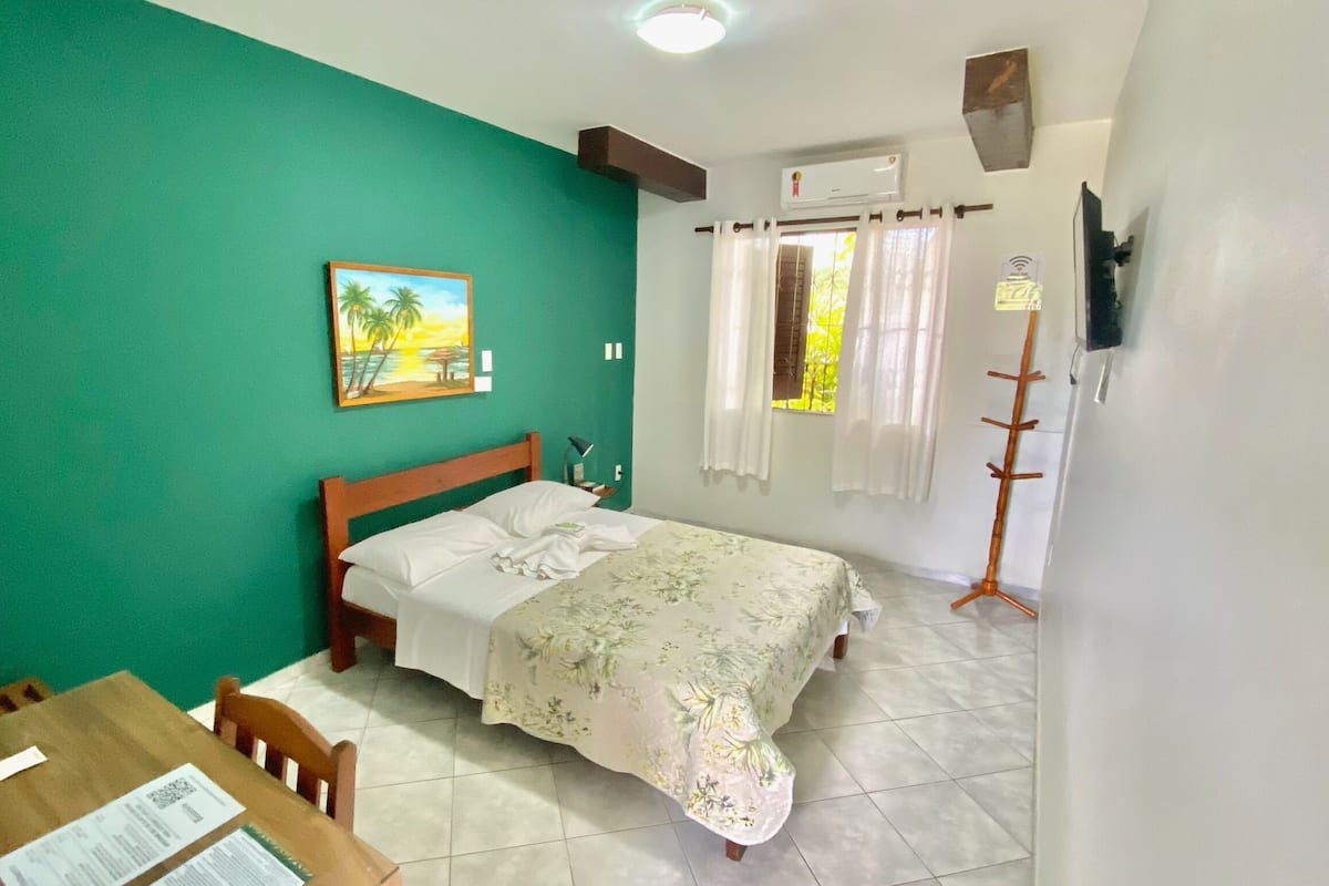 Une chambre à coucher comprenant un lit, un bureau, une chaise, un tableau, un climatiseur et un porte-manteau.