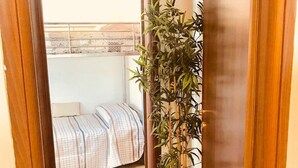A room with a bed, a potted plant, and a view of a balcony.