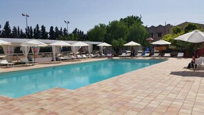 A swimming pool with tiled flooring, sun umbrellas, lounge chairs, and a slide.