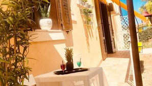 An outdoor seating area with a table and chairs, potted plants, and a small table with drinks.