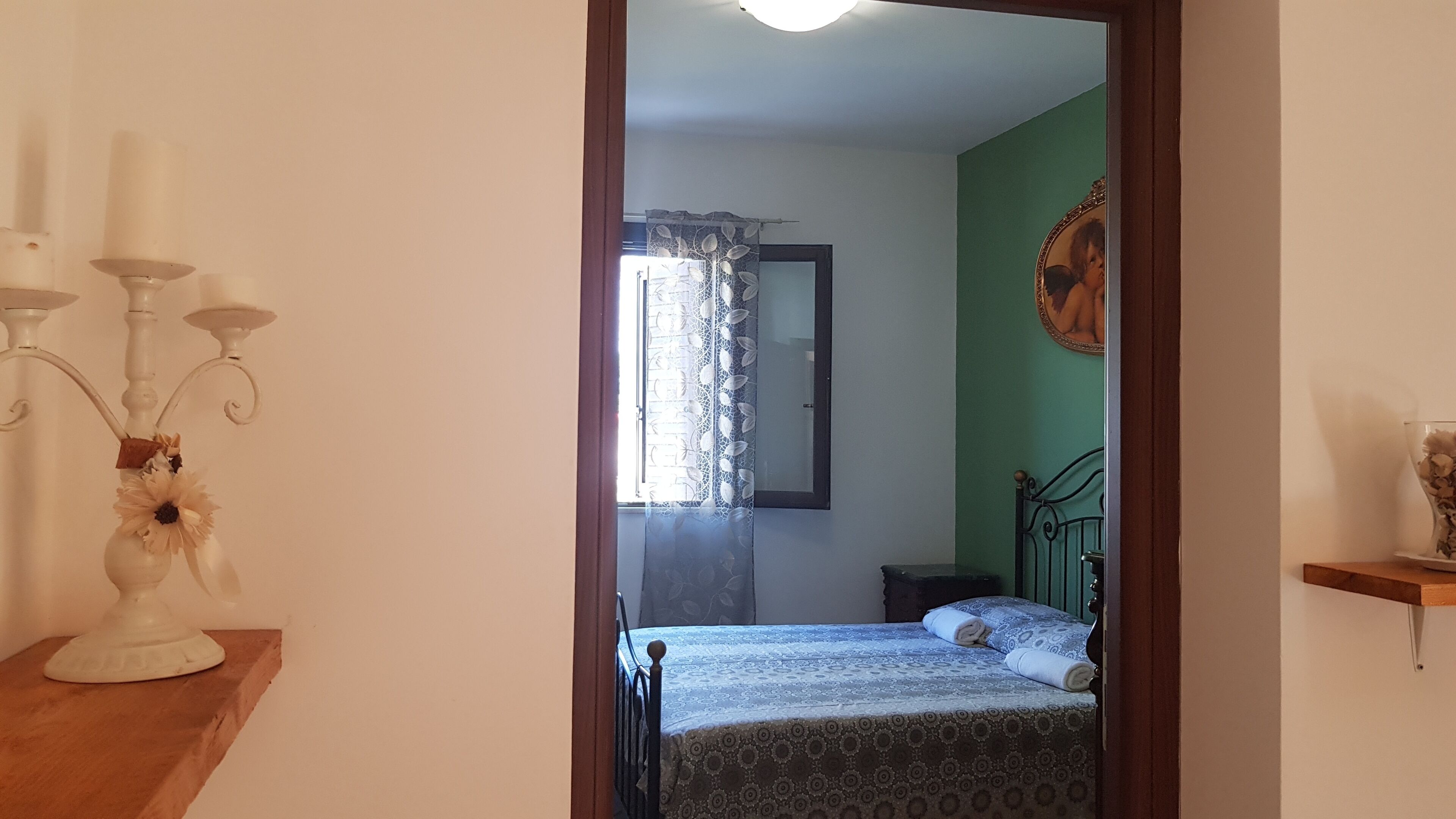 A bedroom with a bed, a nightstand, a mirror, and a window with a curtain.