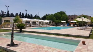 A swimming pool with lounge chairs and umbrellas, surrounded by a tiled deck and greenery.