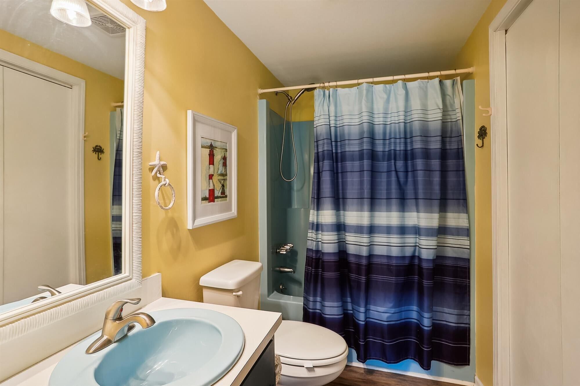 Een badkamer met een blauwe wastafel, een wit toilet en een douchegordijn met een blauw-wit gestreept patroon.