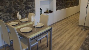 Uma sala de jantar com parede de pedra, uma TV de tela plana fixada acima de uma estante, e uma mesa moderna com cadeiras.
