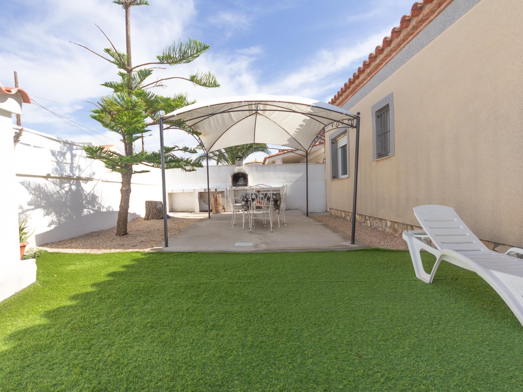 Un jardin avec un espace barbecue, un coin salon abrité et une pelouse.