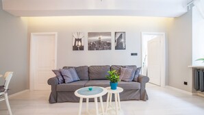 A modern living room with a grey sofa, two white side tables, a potted plant, and three framed cityscape pictures on the wall.