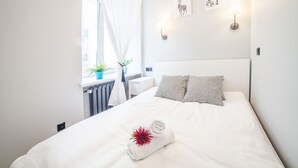 A neatly made bed with a rolled towel, two patterned pillows, and a wall-mounted lamp.