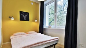 A bedroom with a bed, a window with curtains, a wall-mounted light, and a deer head artwork.