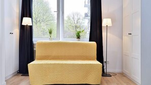 A yellow sofa in a room with a large window, two floor lamps, and a white wardrobe.