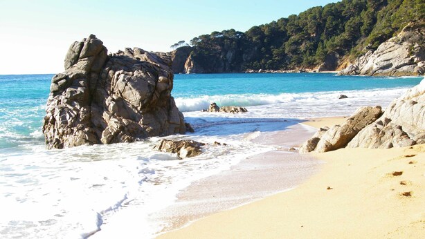 Una playa con formaciones rocosas y agua azul cristalina.
