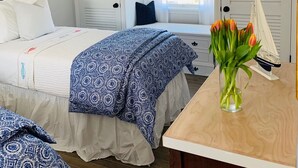 Ett sovrum med en säng, ett nattduksbord, en vas med blommor och en takfläkt.