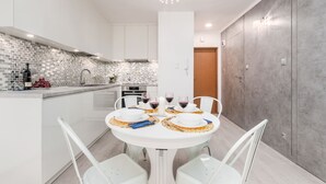 Een moderne keuken met witte kastjes, een betegelde spatwand en een eethoek met een witte tafel gedekt voor vier personen.