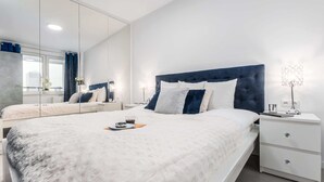 Een moderne slaapkamer met een groot bed, nachtkastje, spiegel en een raam met gordijnen.