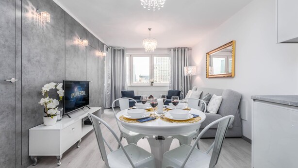 Een moderne eetruimte met een ronde tafel, witte stoelen en een kroonluchter.