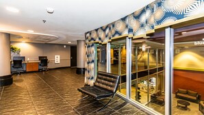 A lobby with a reception desk, two black office chairs, a bench, and a glass partition with a view of a seating area. - Las Vegas | Vegas Nightlife Stay | Pool & Hot Tub | 1BR (Las Vegas)