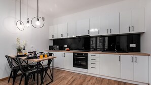 Une cuisine moderne avec des meubles blancs, des appareils électroménagers noirs et une table à manger en bois, assortie de chaises.
