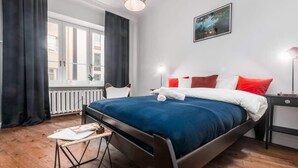 Un dormitorio moderno con una cama grande, una ventana con cortinas, una mesita de noche y una lámpara.