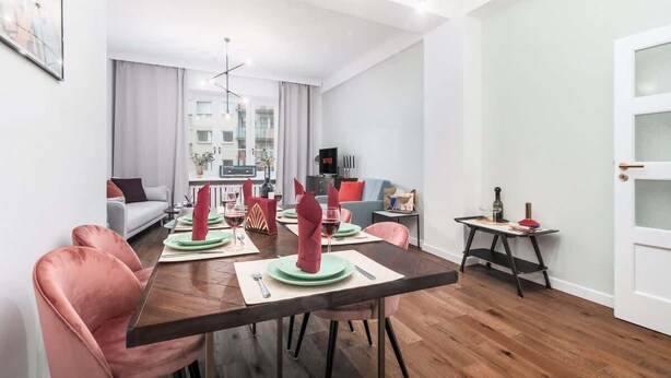 Una sala de estar moderna con comedor, un sofá, un televisor y una pequeña mesa con una botella y vasos.