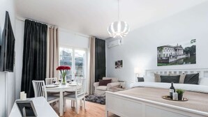 A modern hotel room with a bed, a dining table with chairs, a TV, and a large window with curtains. - Stylish Apartment | Air Conditioning | Close Center (Warszawa)