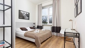 A modern bedroom with a bed, a desk, a window with curtains, and a framed picture on the wall. - A Unique Apartment with a Balcony & Parking | Close to Łazienki Królewskie (Warszawa)