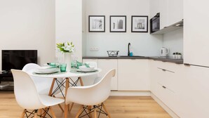 A modern kitchen with white cabinets, a dining table with white chairs, and three framed pictures on the wall. - A Unique Apartment with a Balcony & Parking | Close to Łazienki Królewskie (Warszawa)