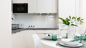 A modern kitchen with white cabinets, a black oven, and a dining area with a white table set for two. - A Unique Apartment with a Balcony & Parking | Close to Łazienki Królewskie (Warszawa)