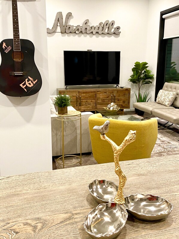 Una sala de estar con televisión, guitarra, sillón amarillo y una escultura decorativa.