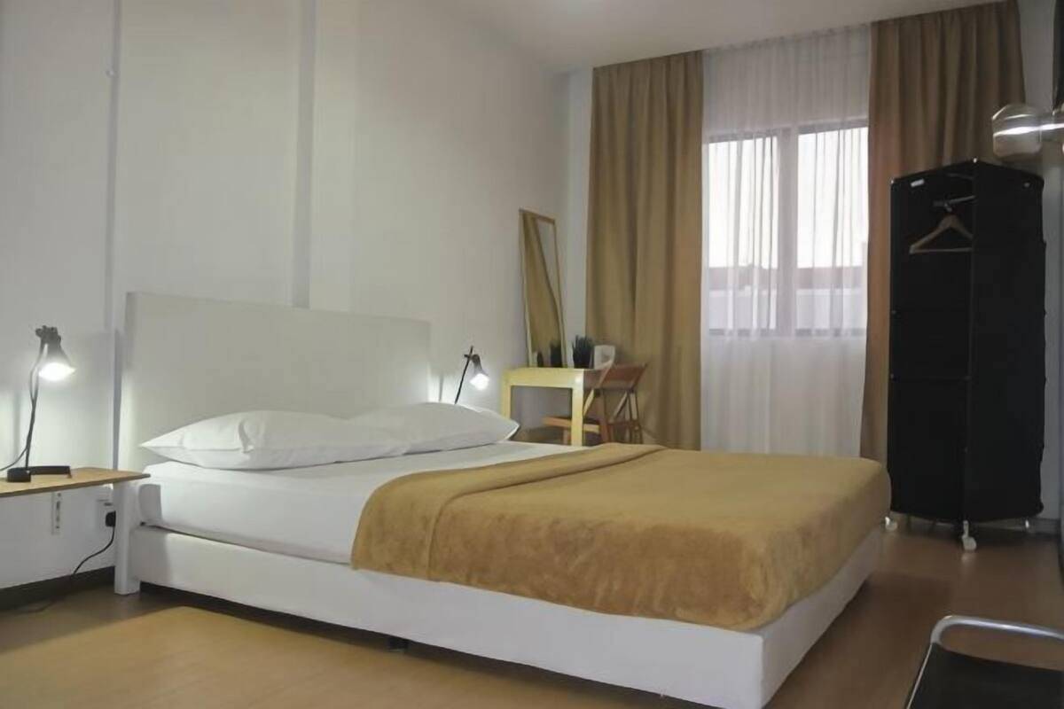 A hotel room with a bed, bedside table, lamp, and a wardrobe.
