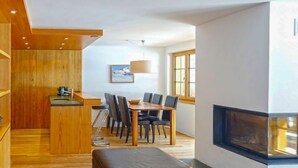 Eine moderne Küche mit Holzausstattung, ein Essbereich mit Tisch und Stühlen sowie ein Kamin.