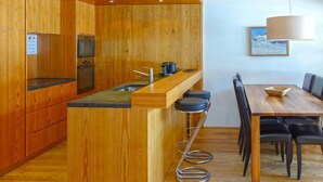 Eine moderne Küche mit Holzschränken, einer zentralen Kochinsel mit Barhocker und einem Essbereich mit Tisch und Stühlen.