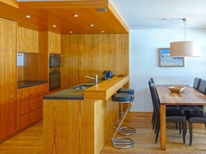 Une cuisine moderne avec des meubles en bois, un îlot central doté de tabourets, et un coin repas avec une table et des chaises.