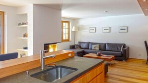 Eine moderne Küche mit Spüle und Holzausbau, ein graues Sofa und ein kleiner Tisch in einem hellen Wohnbereich mit Holzboden.
