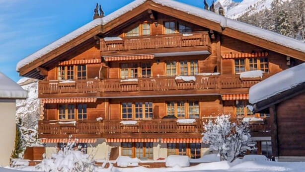 Ein mehrstöckiges Holzchalet mit Balkonen, umgeben von Schnee.