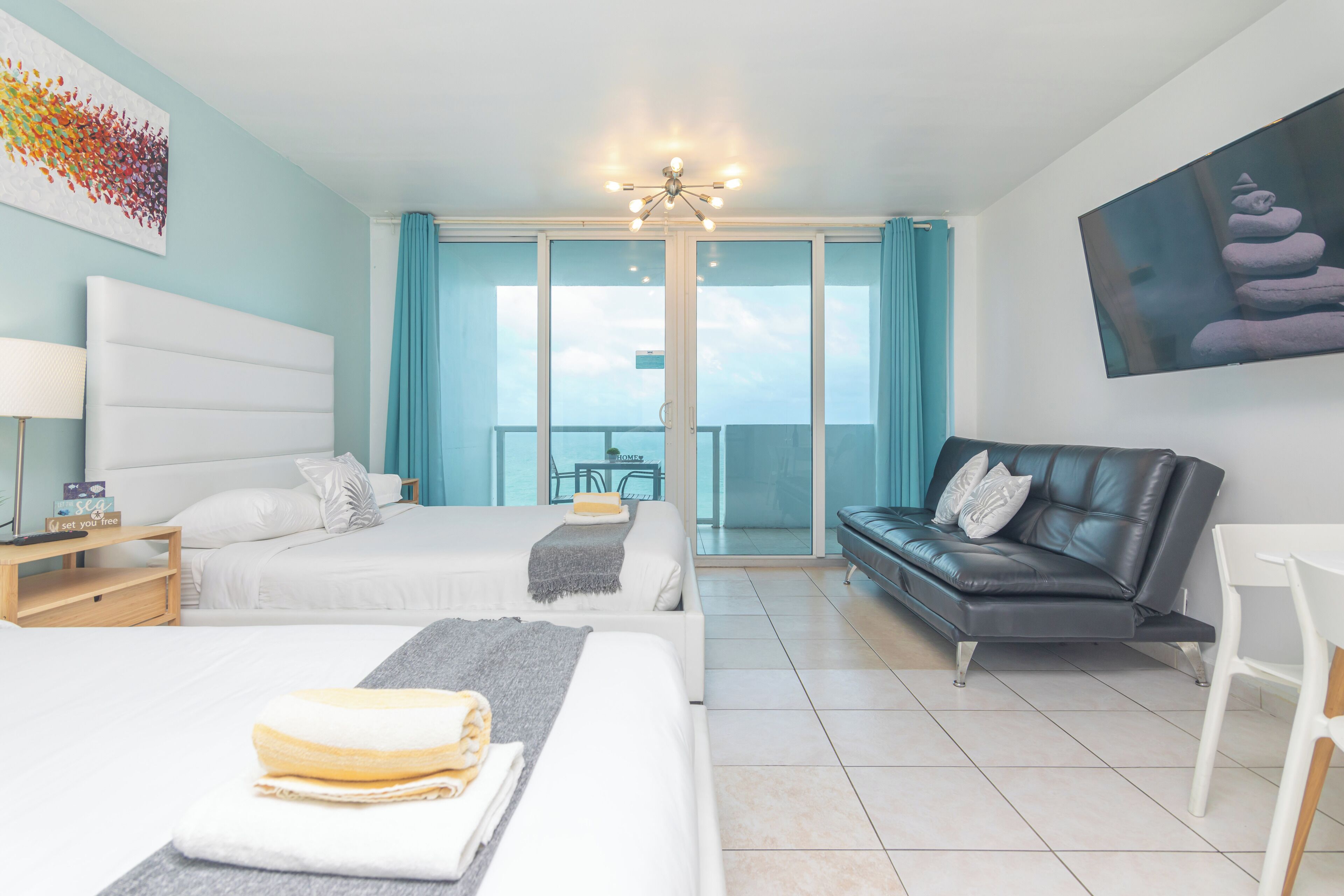 A hotel room with two beds, a sofa, a dining table, and a balcony with a view.