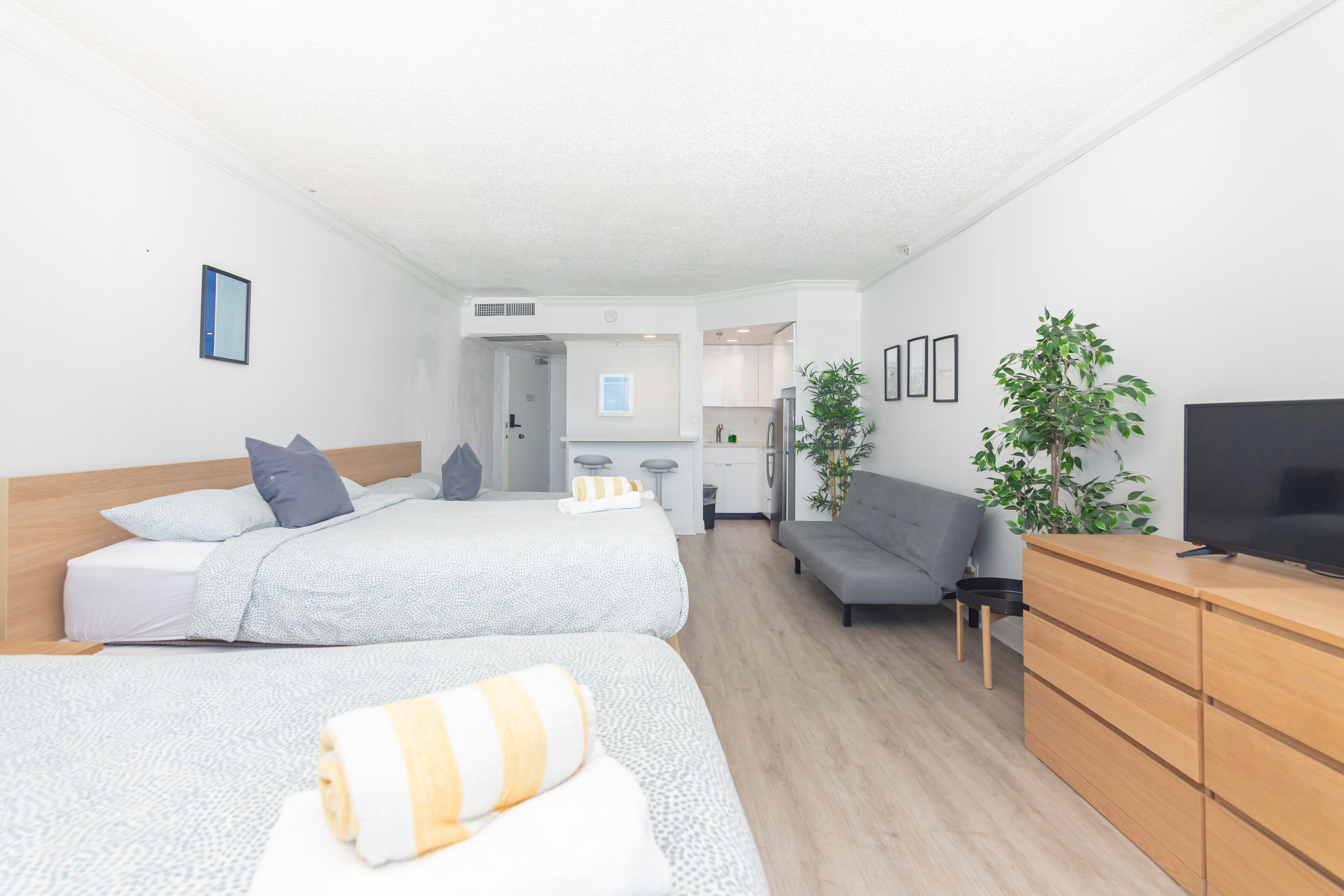 Ein modernes Hotelzimmer mit zwei Betten, einer Couch, einem Fernseher und einer Küchenzeile.
