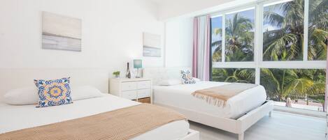 A hotel room with two beds, a large window with a view of palm trees, and a white color scheme.