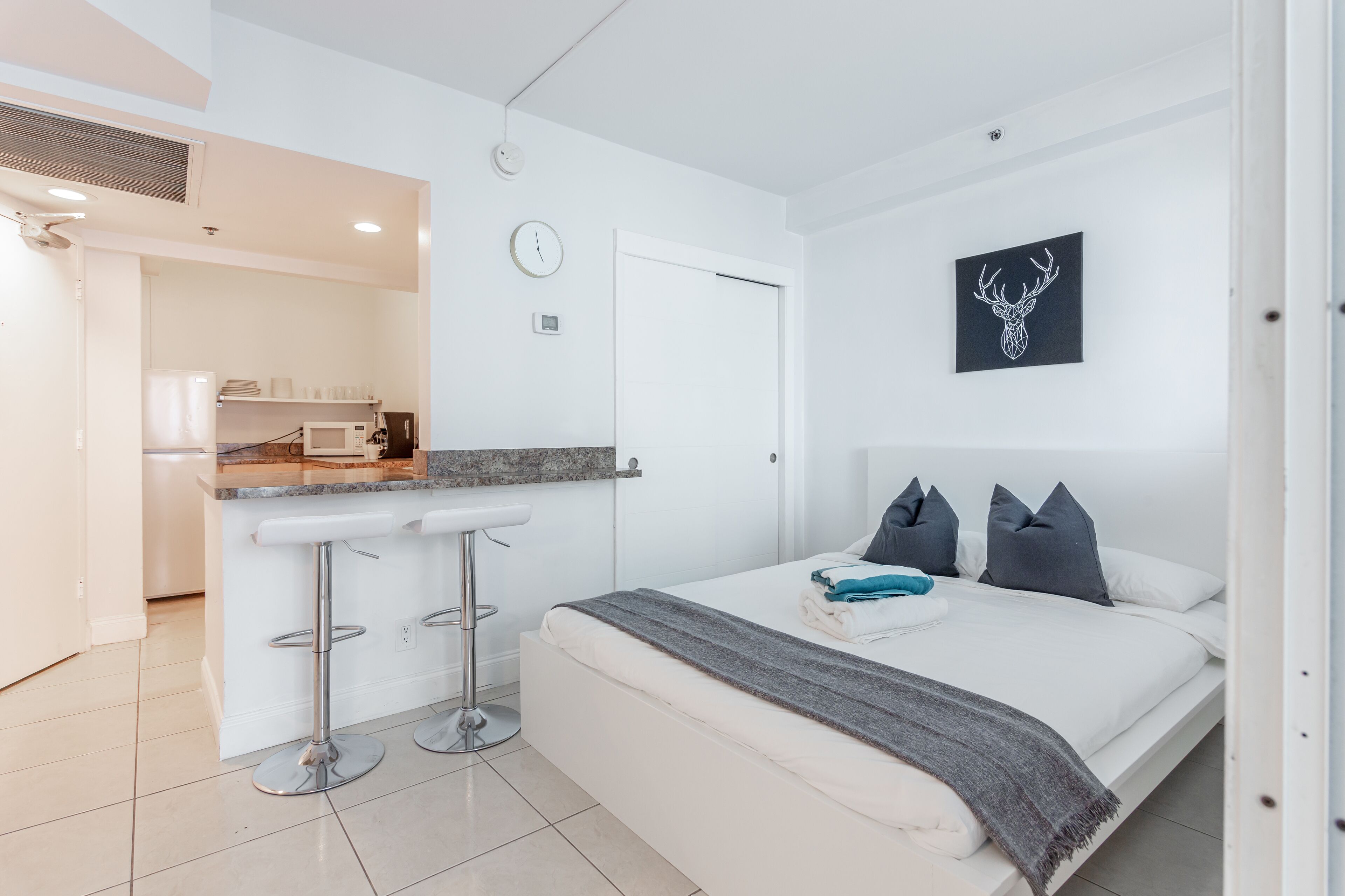 A modern hotel room with a bed, a small kitchenette, and a bathroom.