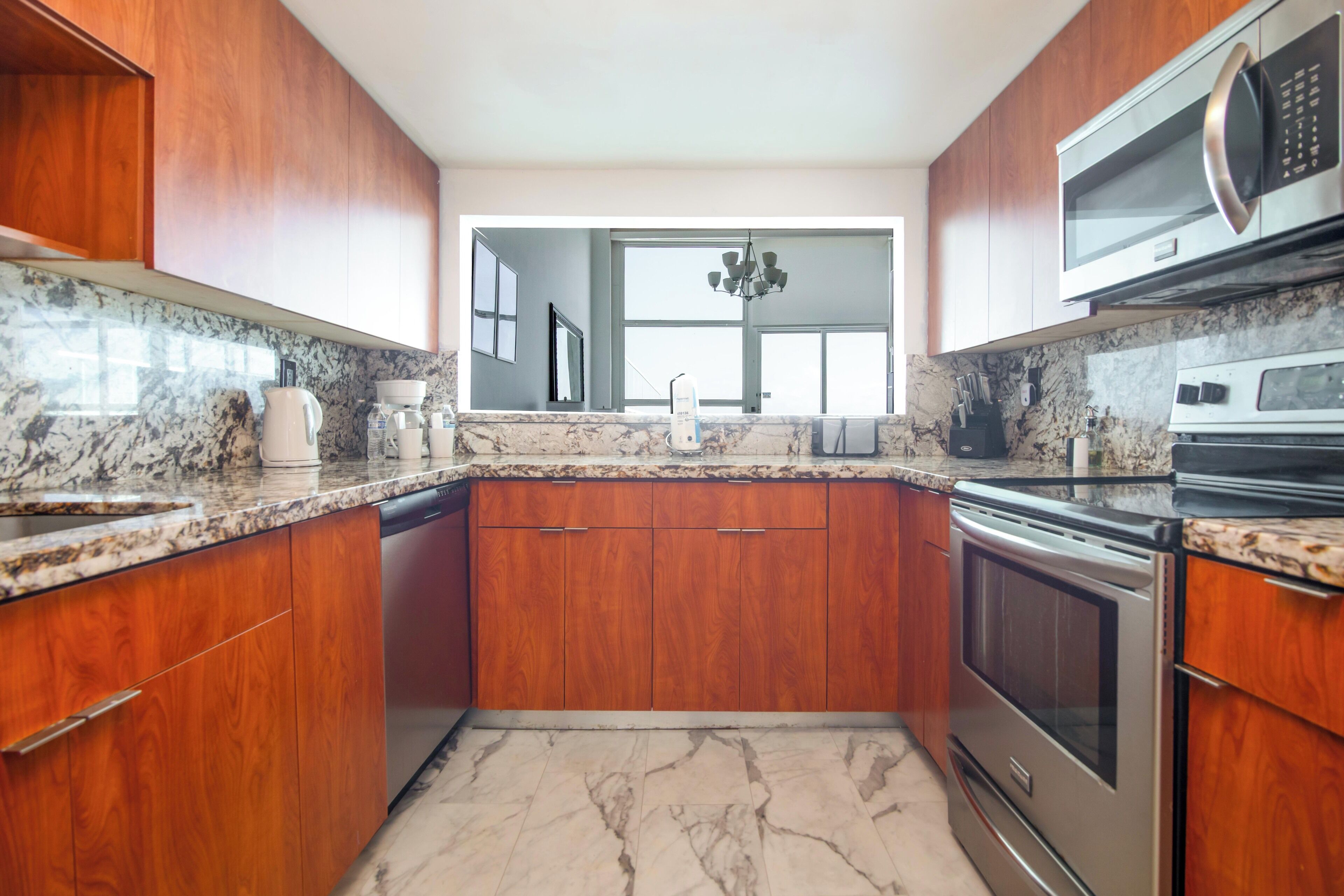 A modern kitchen with wooden cabinets, granite countertops, stainless steel appliances, and a large window providing natural light.