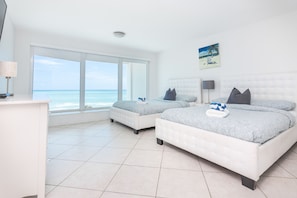 A hotel room with two beds, a desk, and a large window offering a view of the ocean.